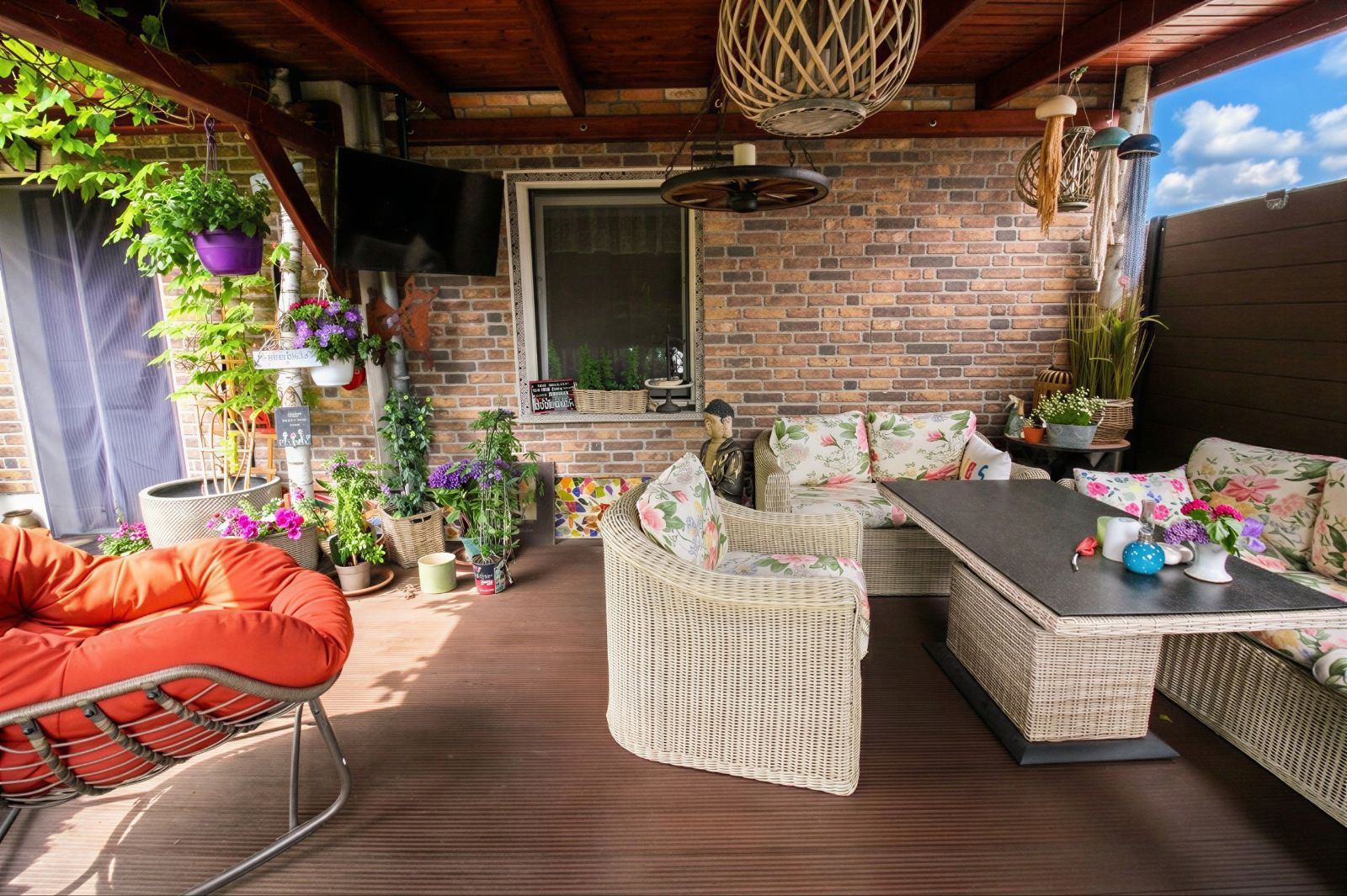 Überdachte Terrasse mit Sitzmöbeln, Holzboden, Pflanzen und Wand aus Backstein.
