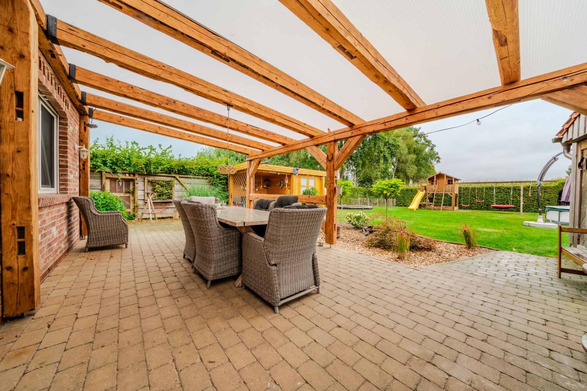 Überdachte Terrasse mit Sitzgruppe und Blick auf Garten mit Spielplatz.