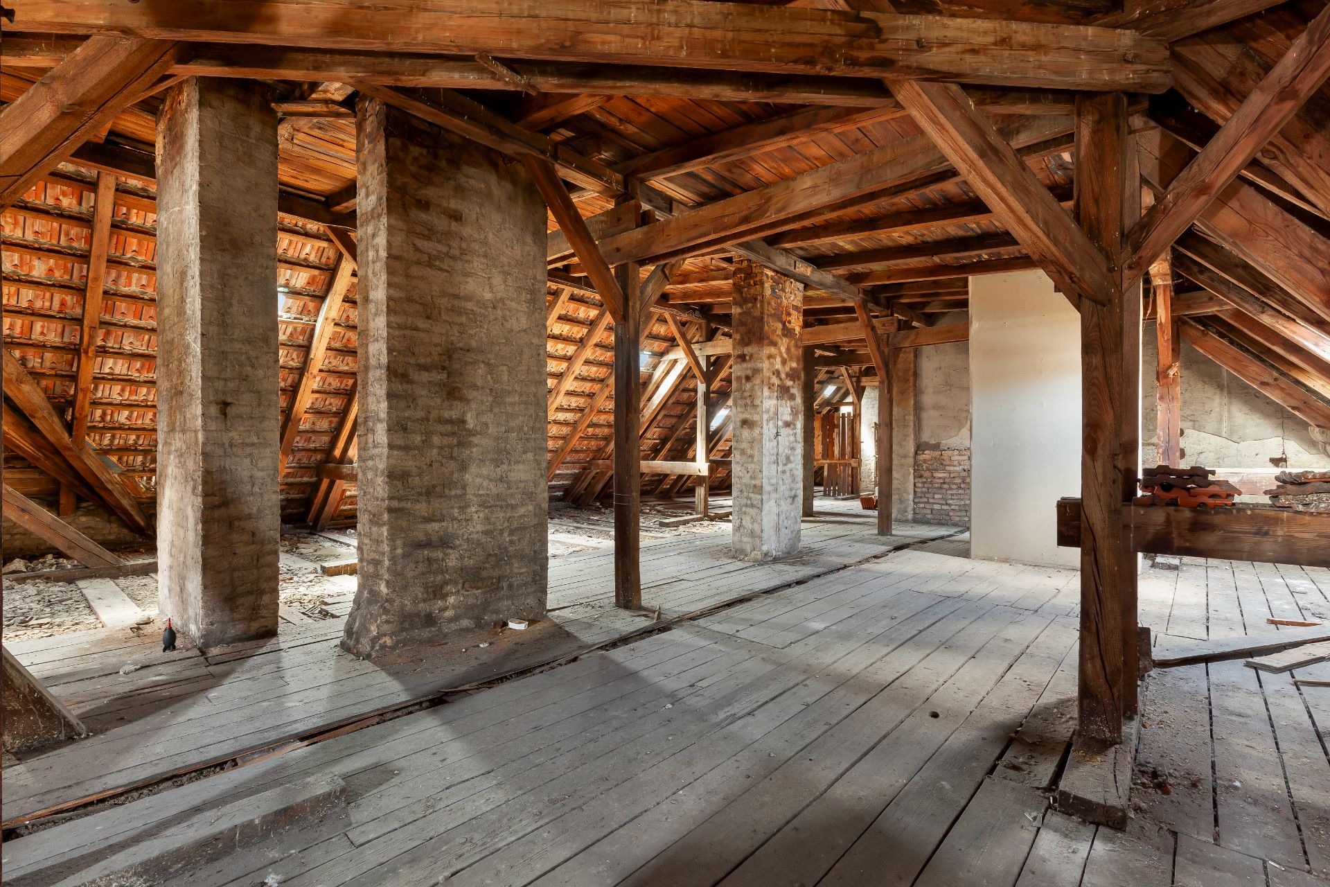 Alter Dachboden mit Holzbalken, Holzboden und gemauerten Stützen, sichtbar sind Dachschrägen und offene Strukturen.