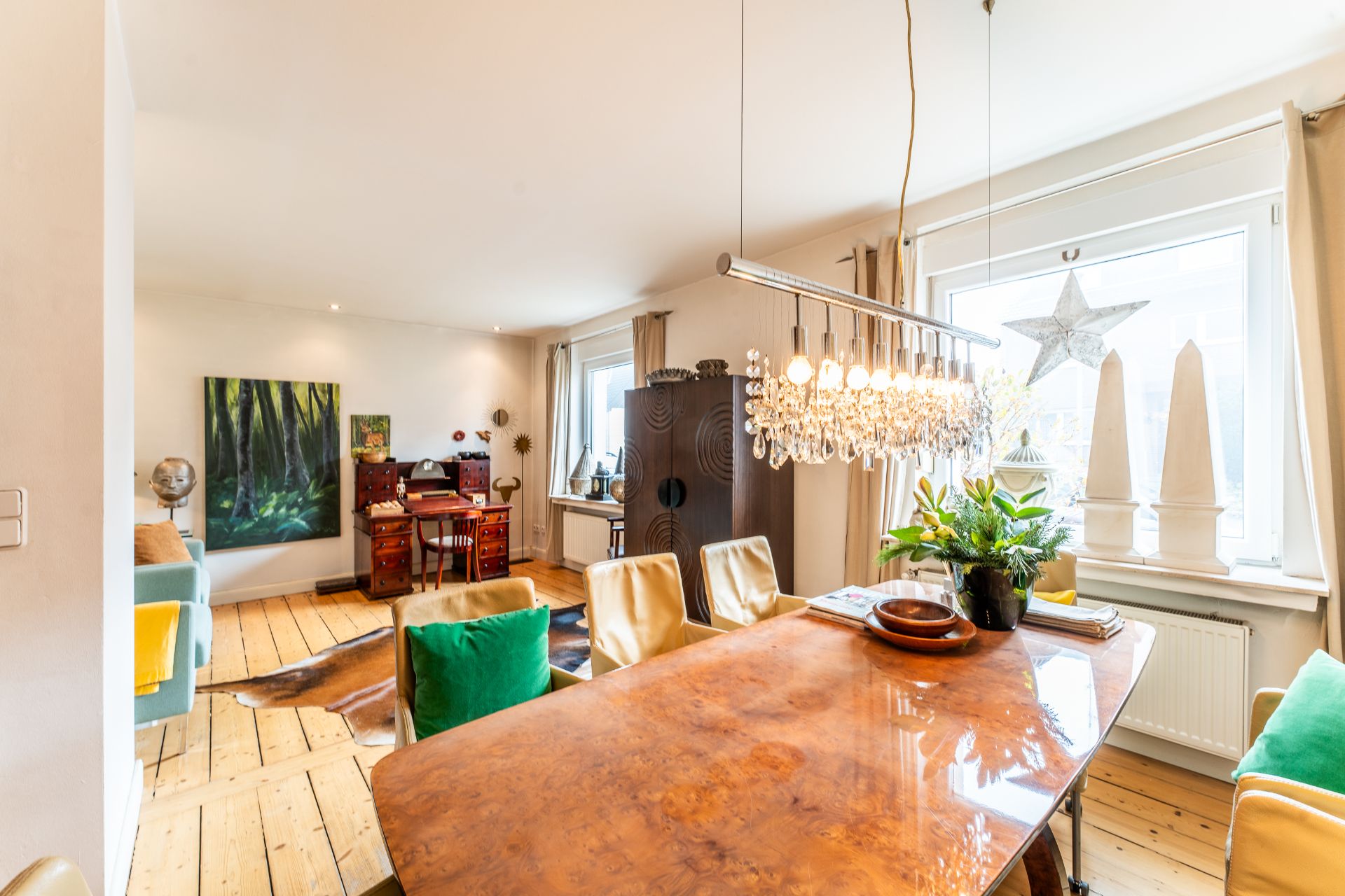 Helles Wohnzimmer mit Esstisch, Kronleuchter, Pflanzen und Fenster mit Dekoration.