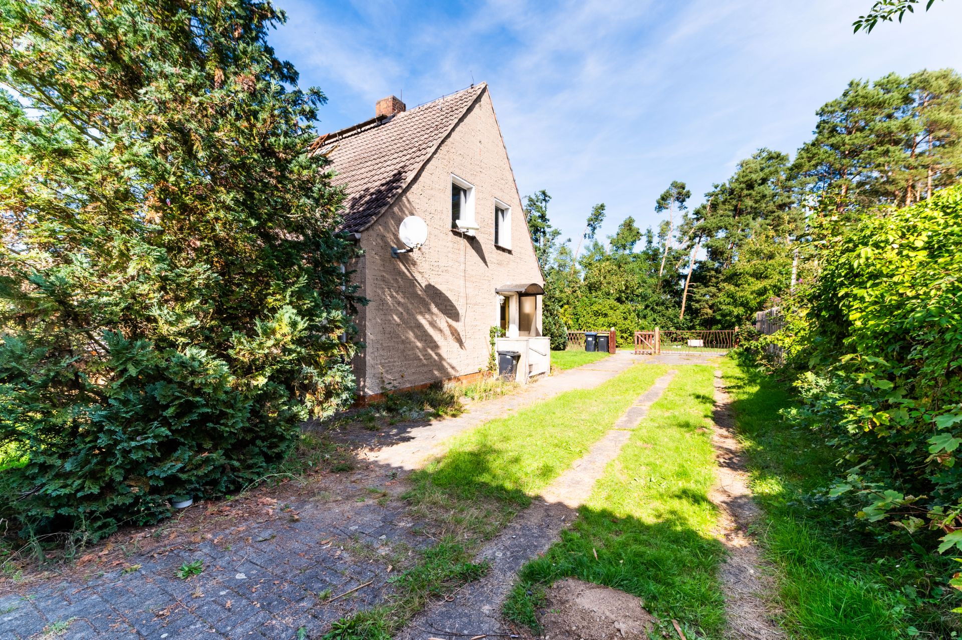 Zweistöckiges Haus mit Garten, von Bäumen und Sträuchern umgeben, Einfahrt sichtbar.