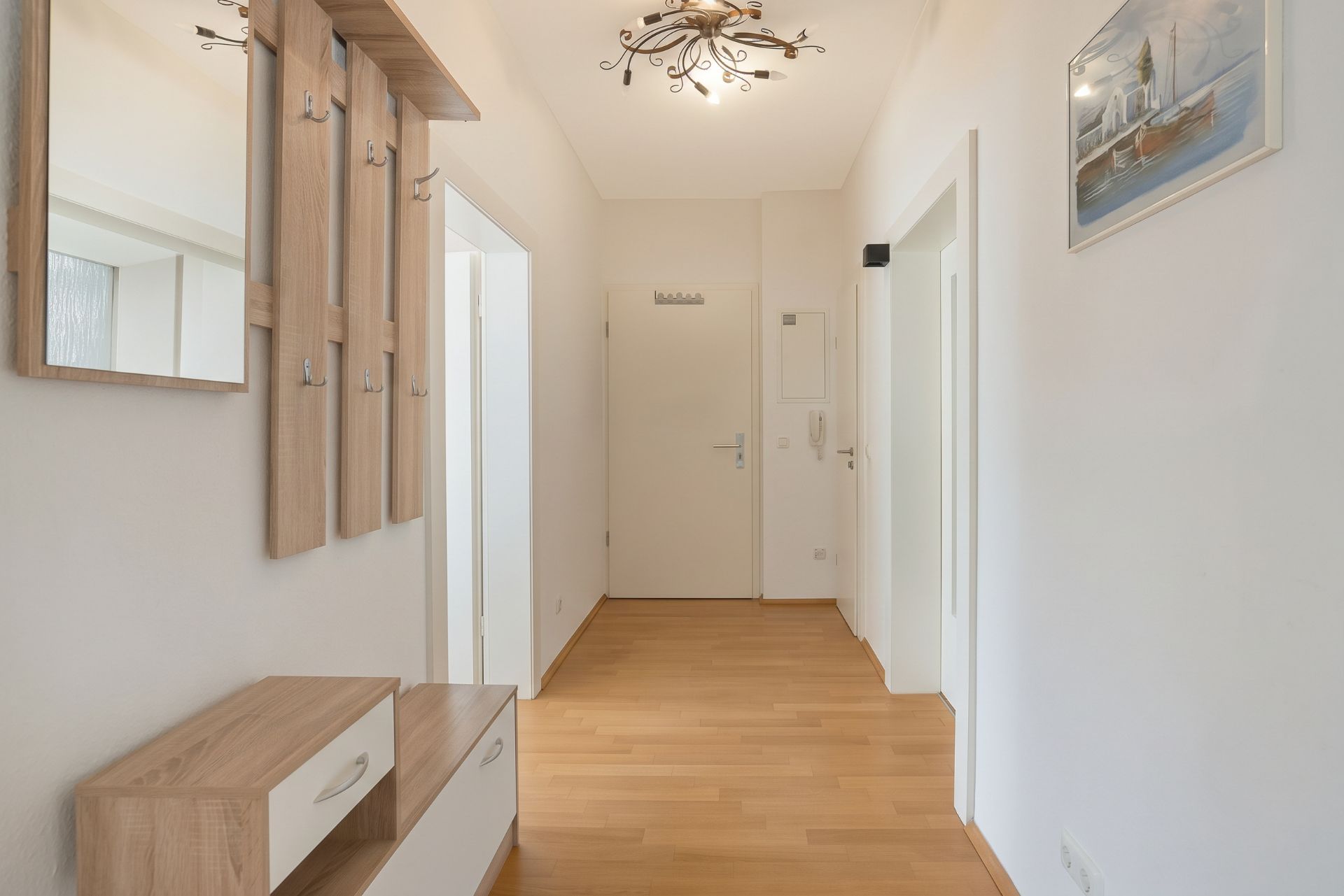 Heller Flur mit Holzfußboden, Garderobe, Spiegel und Deckenleuchte.