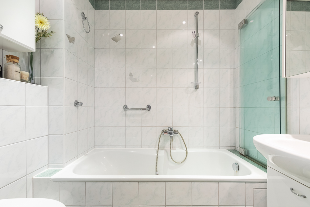 Modernes Badezimmer mit Badewanne, weißen Fliesen und Glasduschwand.