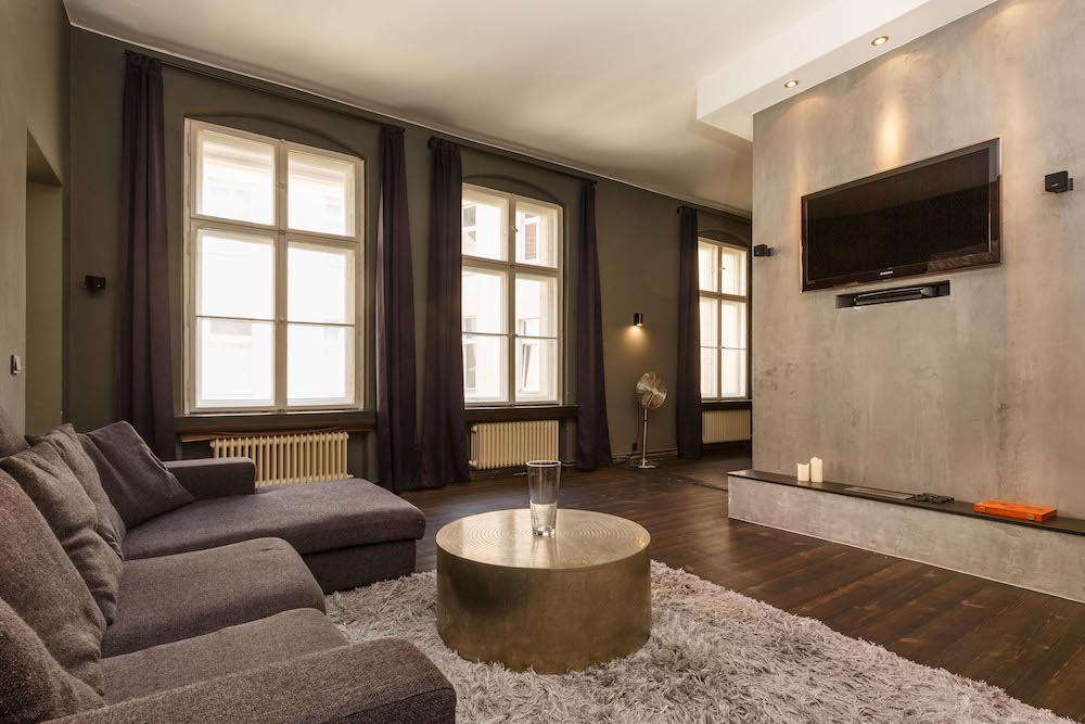 Modernes Wohnzimmer mit grauem Sofa, rundem Tisch, großem Teppich und Wandfernseher.