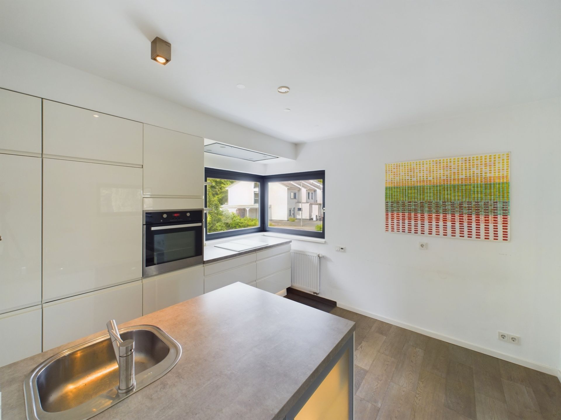 Moderne Küche mit Einbaubackofen, großem Fenster, Waschbecken und bunter Wandkunst.