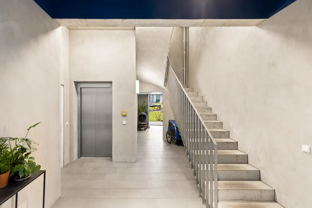 Moderner Hausflur mit Aufzug, Treppe, Pflanzen und Kinderwagen im Hintergrund.