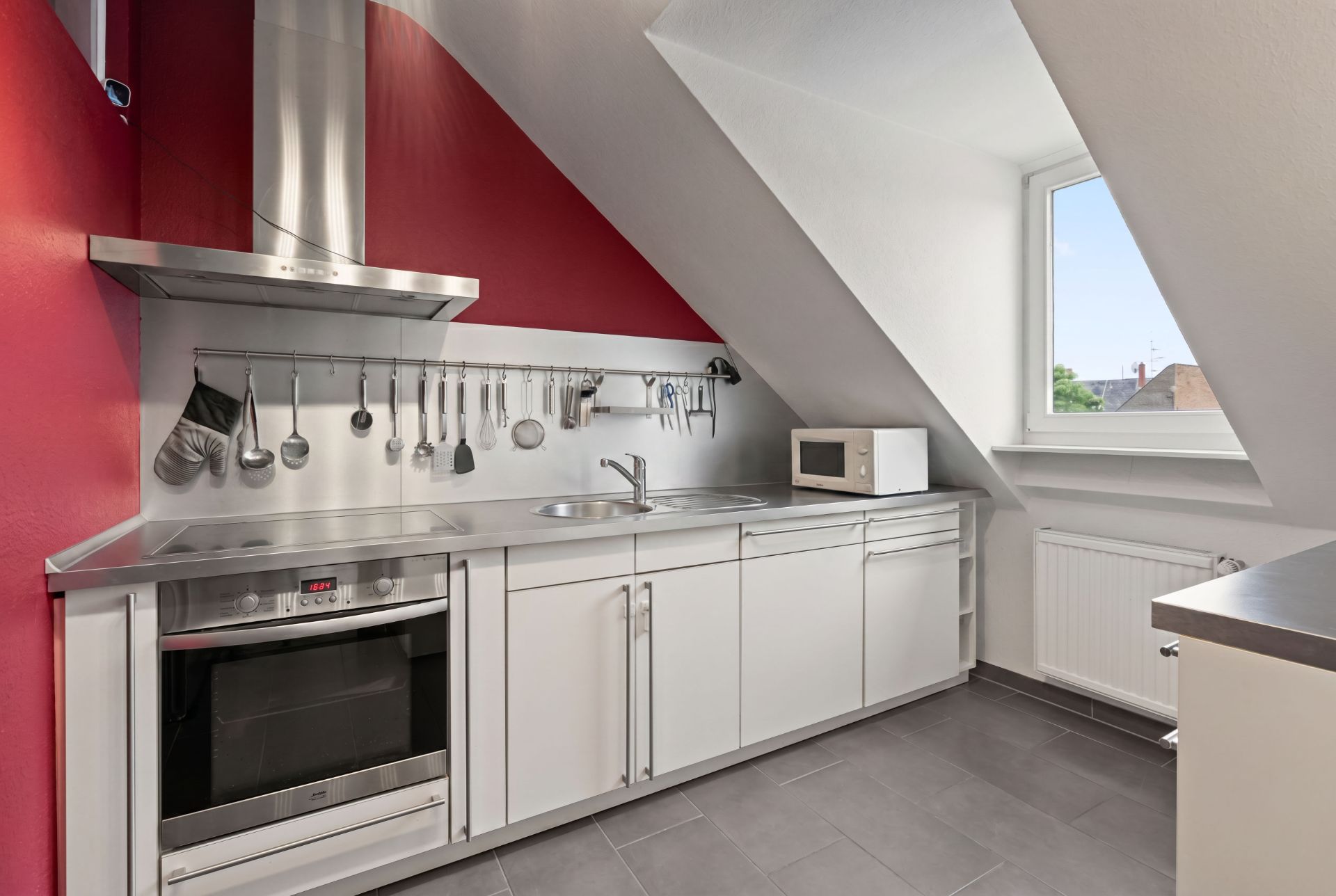 Moderne Dachgeschossküche mit weißen Schränken, Herd, Spüle, Mikrowelle und Utensilienleiste.