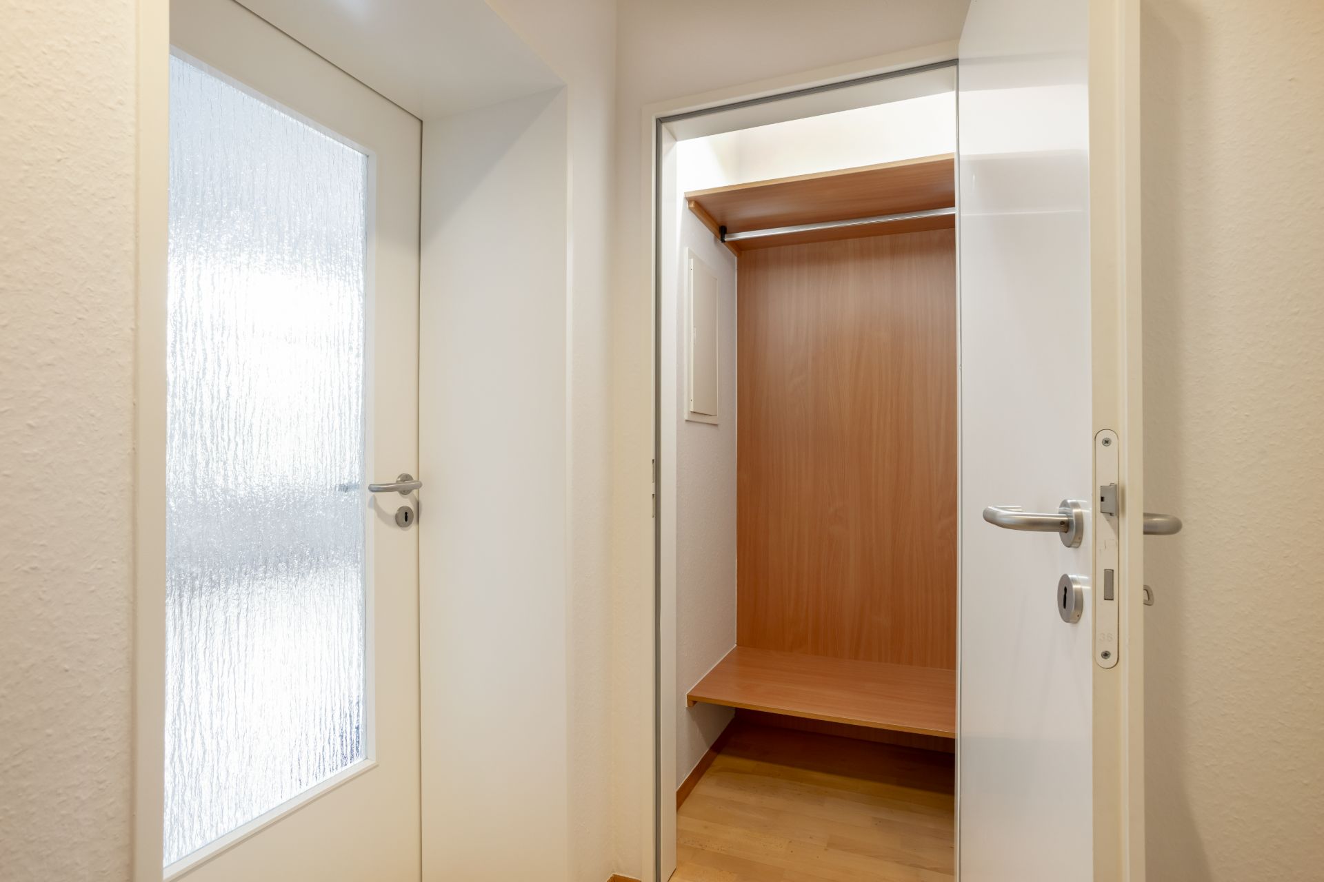 Offene Tür mit Blick in einen leeren Einbauschrank mit Kleiderstange und Regalboden.