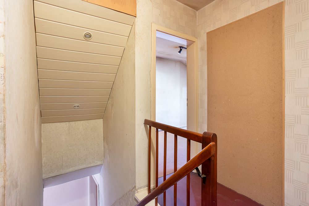 Oberer Treppenabsatz mit Holzgeländer und Tür zu einem Zimmer, Wände mit Tapete.