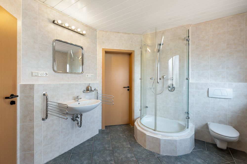 Modernes Badezimmer mit Dusche, Wandwaschbecken, Spiegel und Wandtoilette.