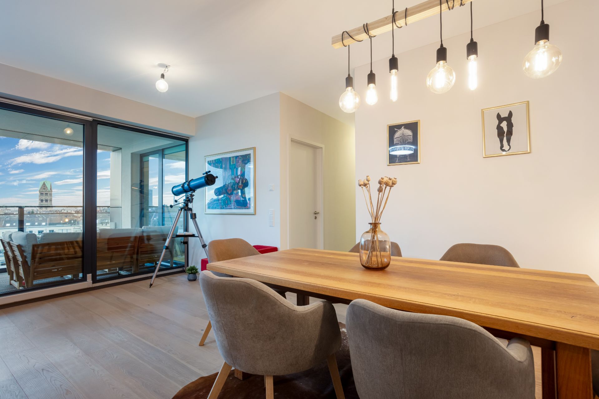 Esszimmer mit Holztisch, vier Stühlen, Hängelampen und Teleskop vor Fenster zur Terrasse.
