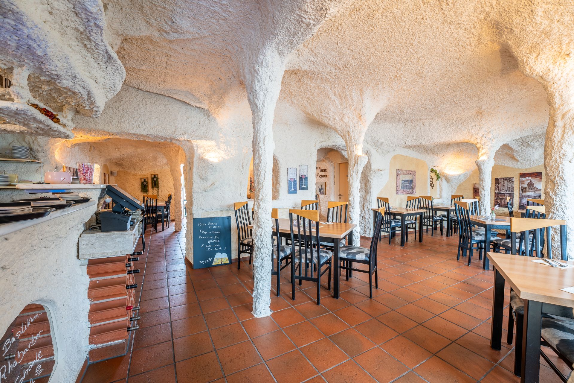 Raum mit Tischen und Stühlen, Höhlenwände und Decke, Fliesenboden.