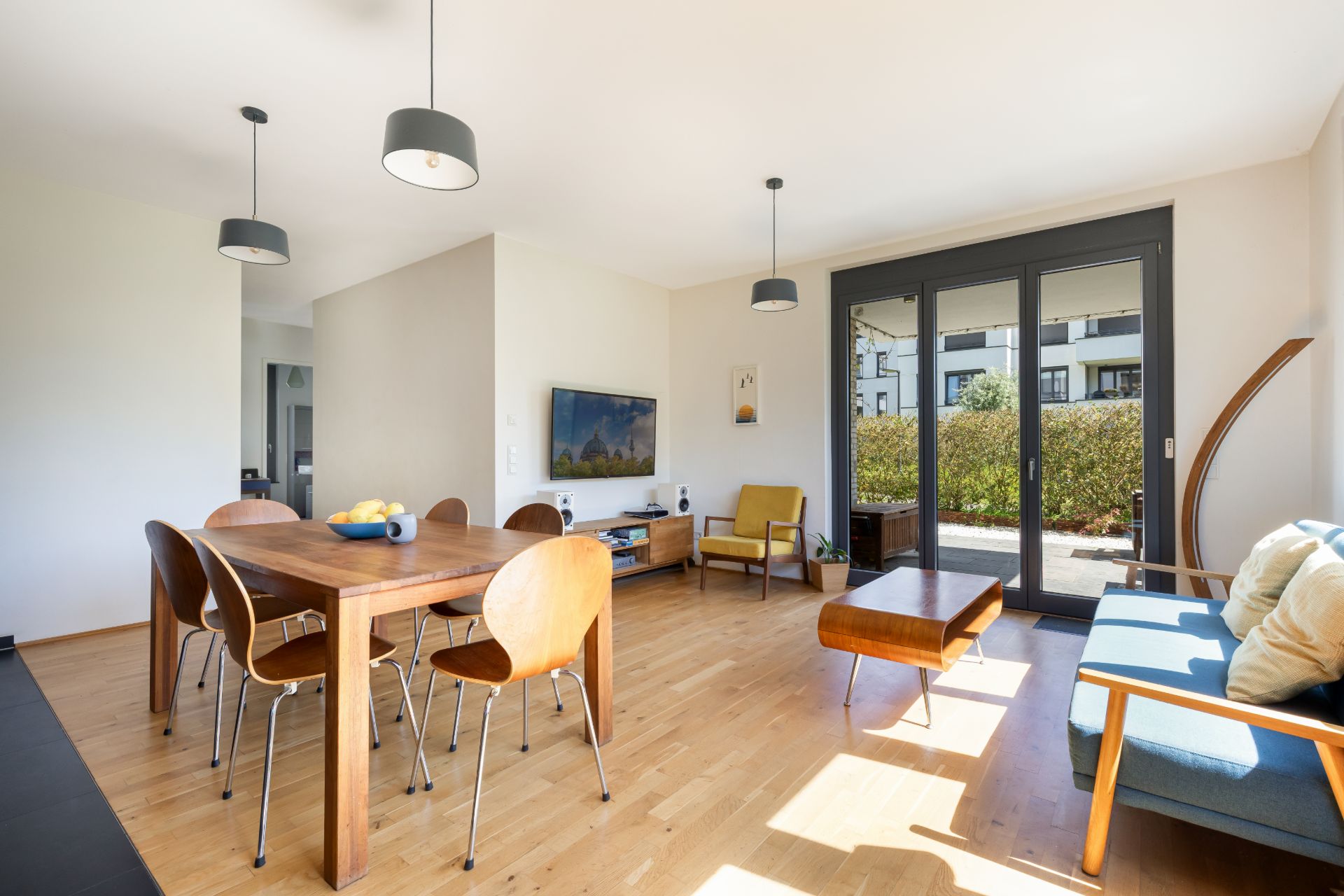 Helles Wohnzimmer mit Holzboden, Esstisch, Sofa, Sessel und großer Fensterfront zum Garten.