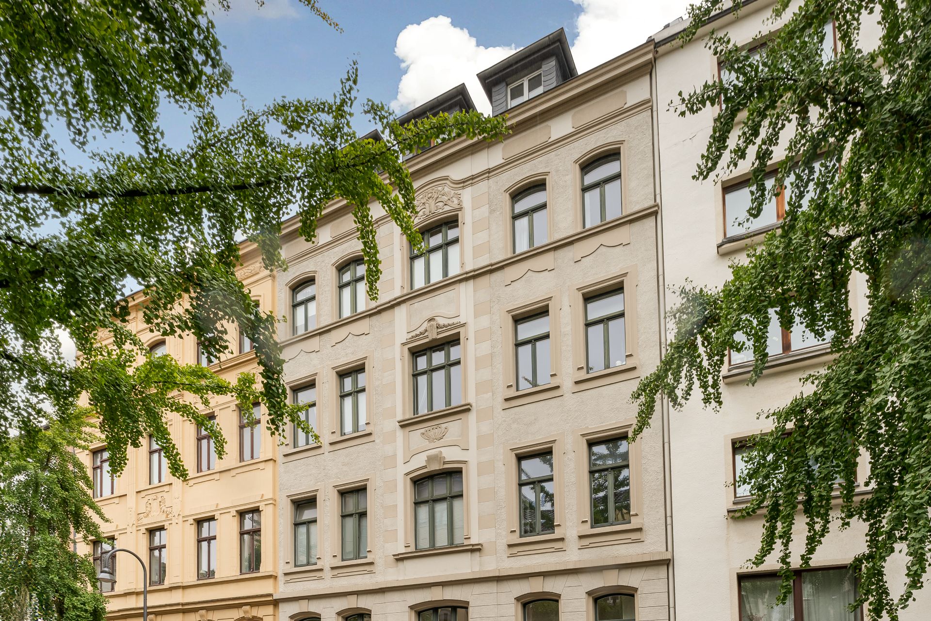 Fassade eines mehrstöckigen Wohnhauses mit klassischen Fenstern, umrahmt von Bäumen.