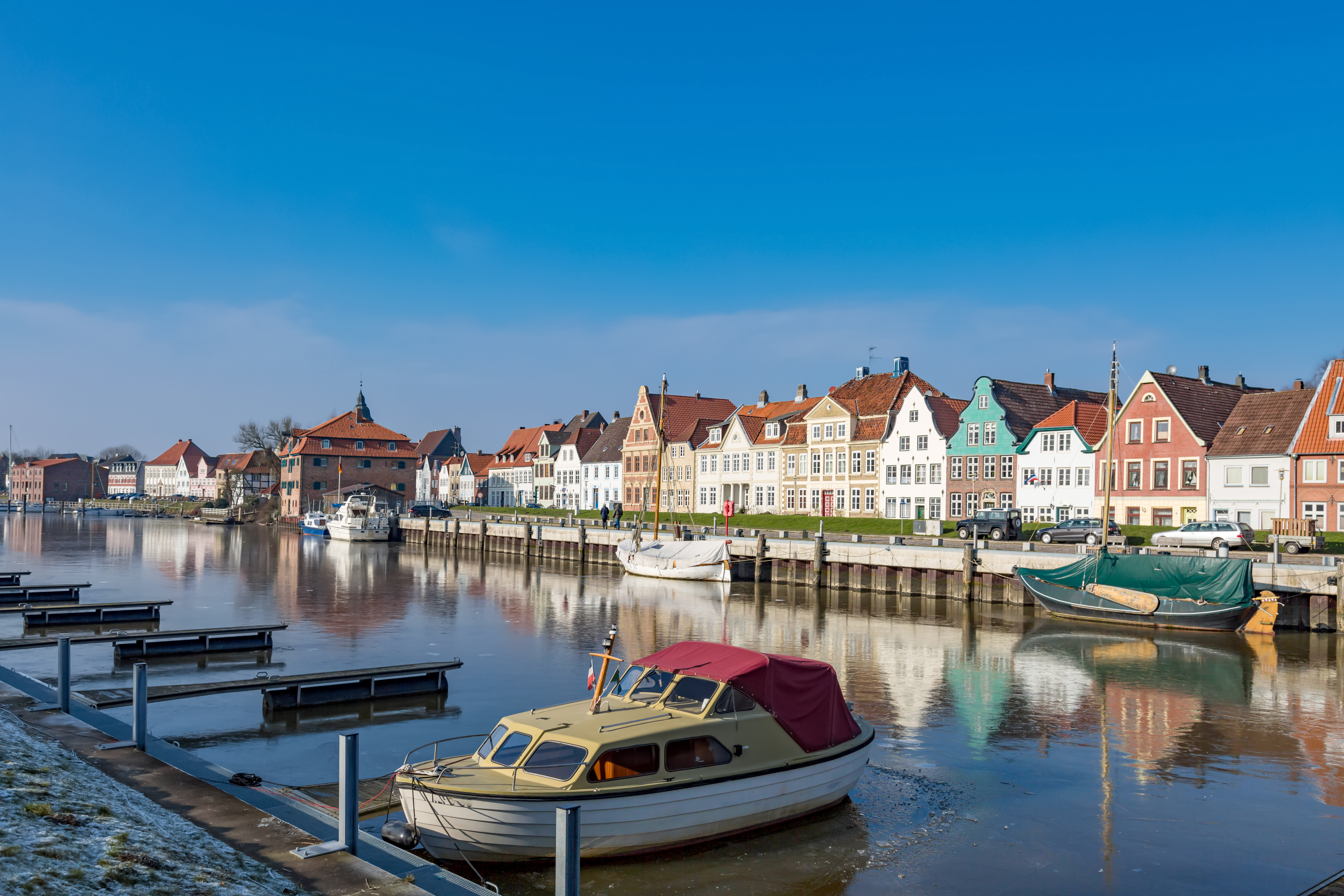 Bunte Wohnhäuser am Flussufer mit Booten im Wasser und blauem Himmel.