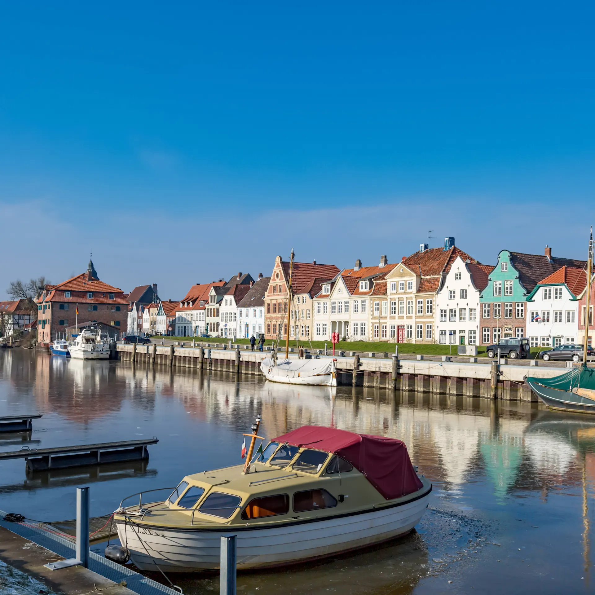 Bunte Wohnhäuser am Flussufer mit Booten im Wasser und blauem Himmel.