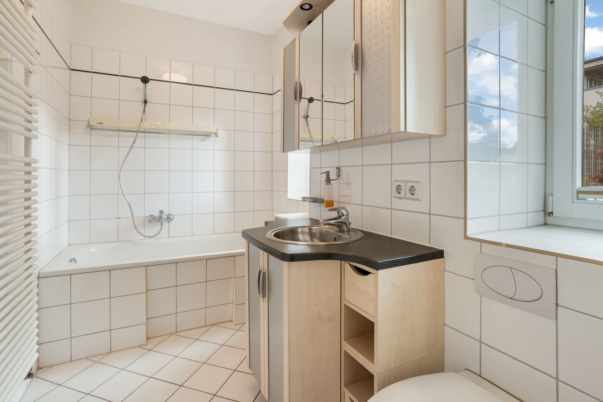 Helles Badezimmer mit Badewanne, Waschbecken, Spiegelschrank und Fenster.