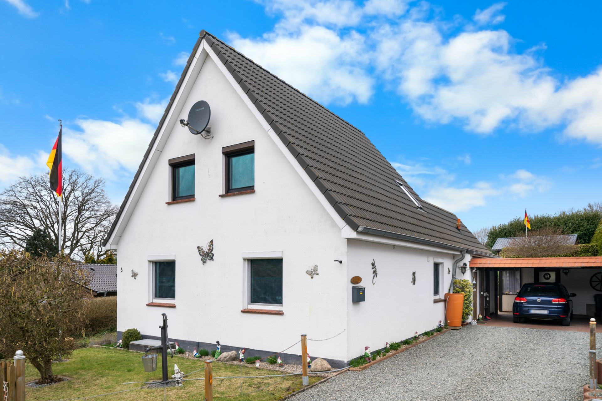 Weißes Einfamilienhaus mit Satteldach, Vorgarten und Auffahrt mit Auto unter Carport.