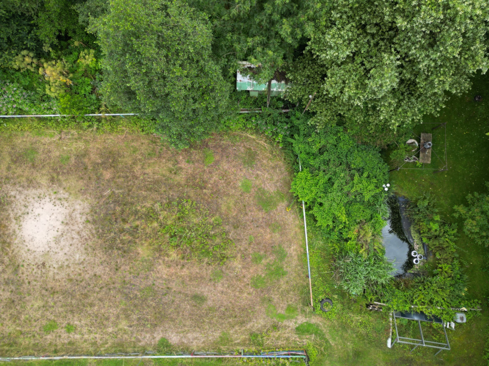 Luftaufnahme eines Gartens mit Wiese, Teich, Bäumen und Gartengeräten.