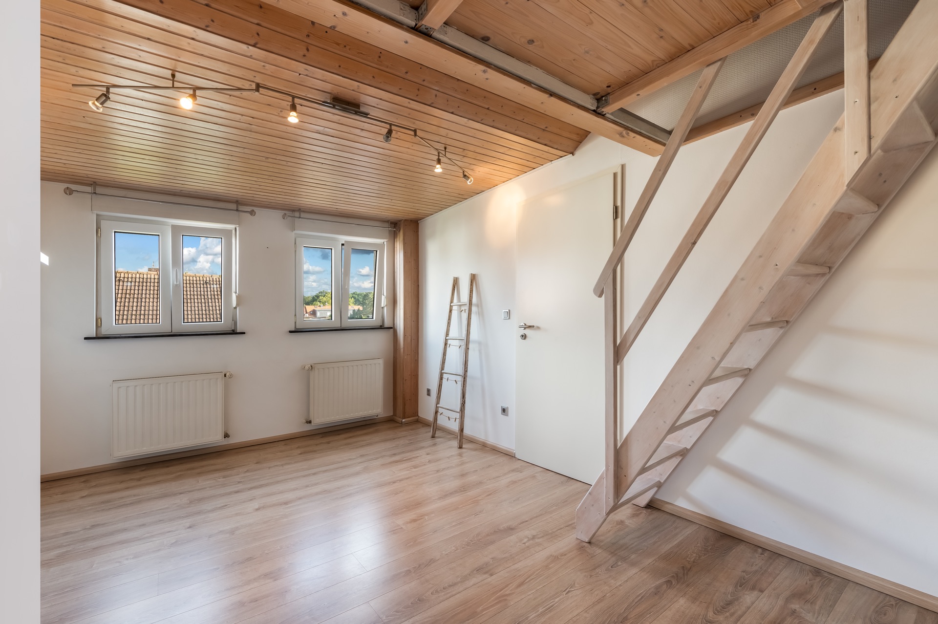 Helles Zimmer mit Holzdecke, zwei Fenstern, Leiter und offener Holztreppe zu einer Galerie.