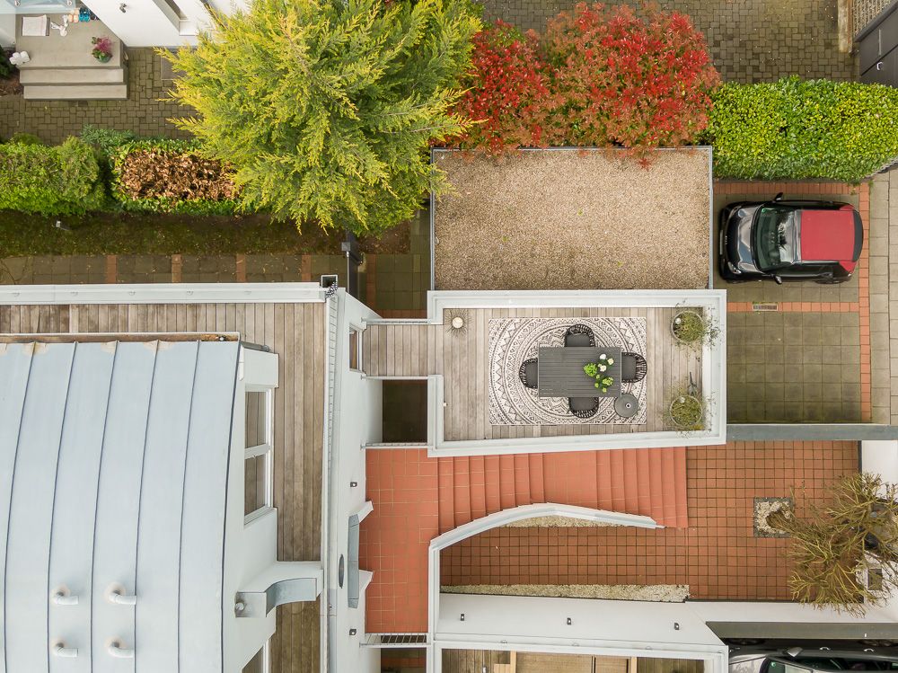 Luftaufnahme eines Gartens mit Tischgruppe, Baum, Parkplatz und roten sowie grünen Büschen.