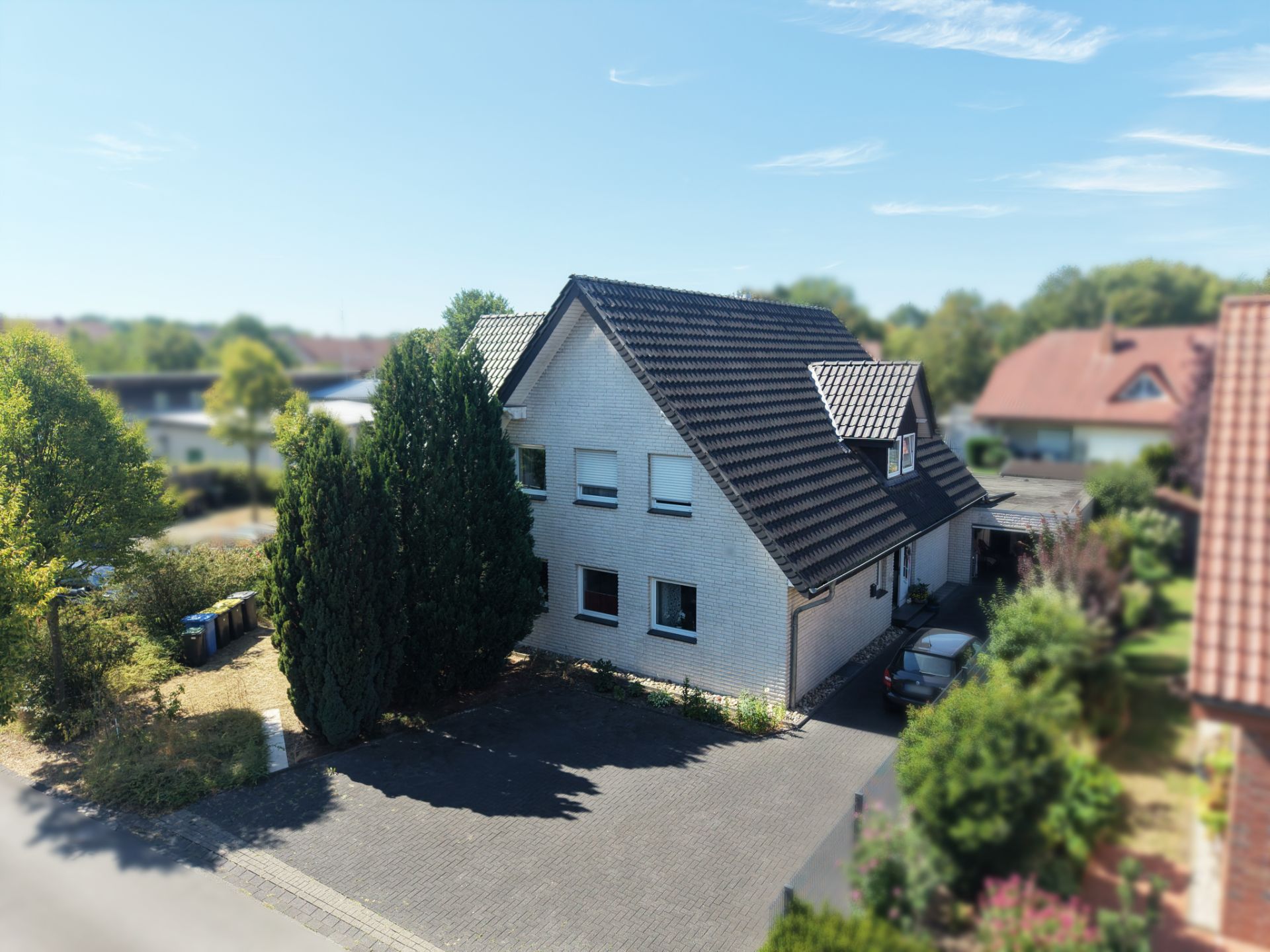 Weißes Einfamilienhaus mit dunklem Dach, Einfahrt und Garten, von Bäumen umgeben.