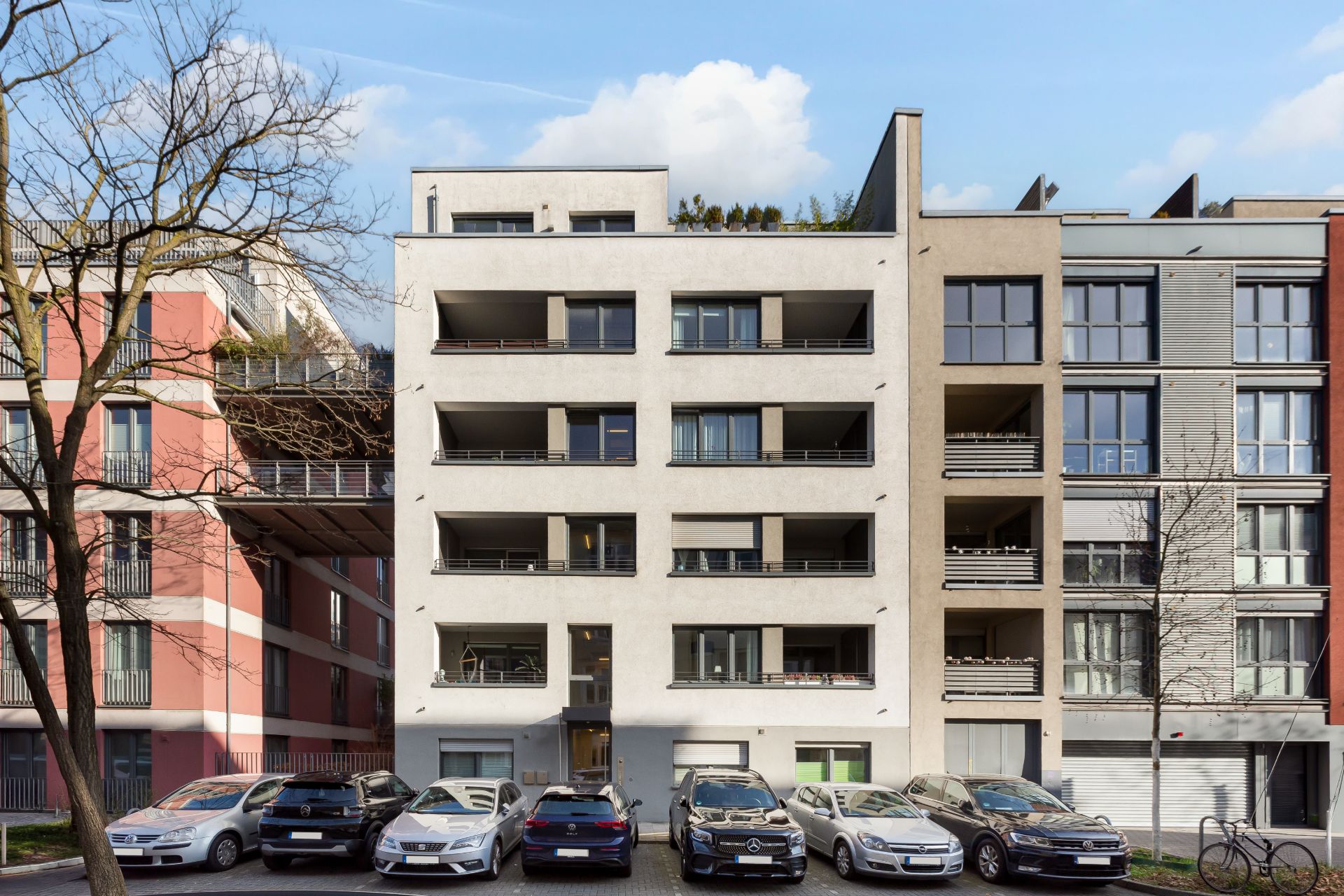 Mehrstöckiges Wohnhaus mit Balkonen und parkenden Autos davor.