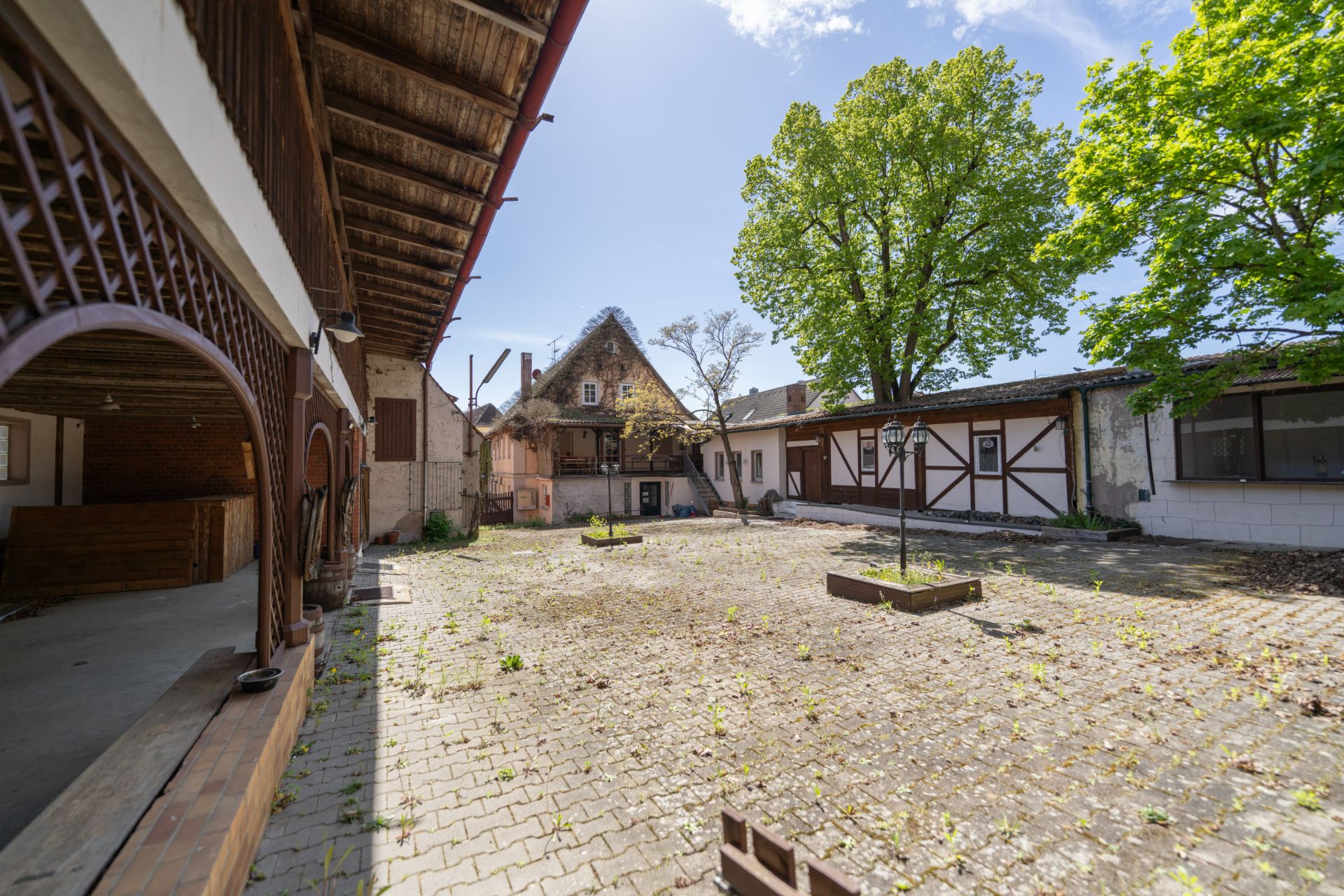 Gepflasterter Innenhof mit mehreren Häusern, Bäumen und überdachtem Bereich auf der linken Seite.