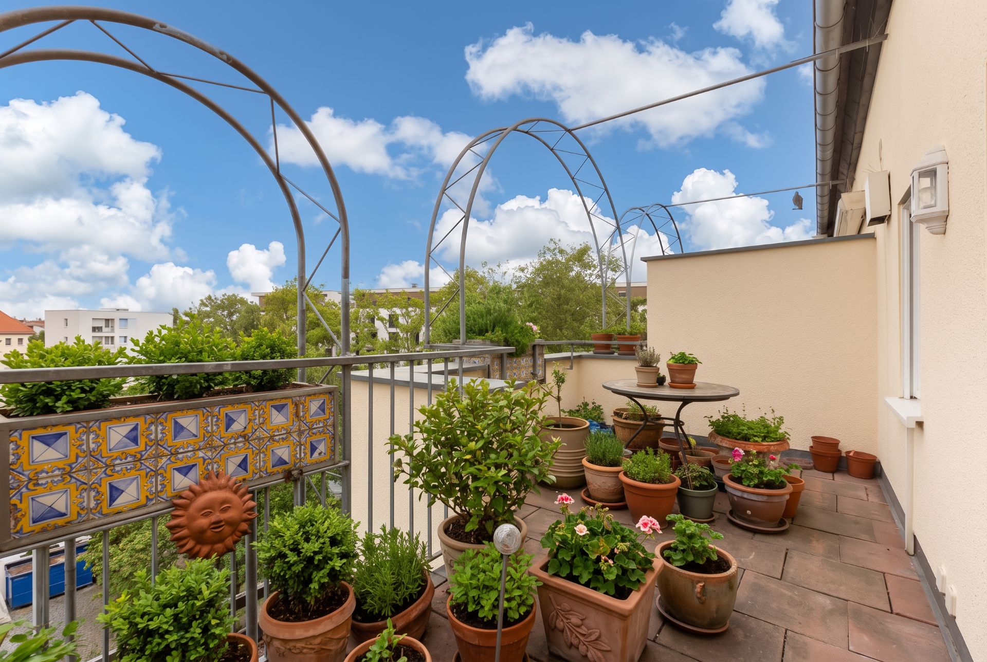Balkon mit vielen Blumentöpfen, kleinem Tisch und dekoriertem Geländer an einem sonnigen Tag.