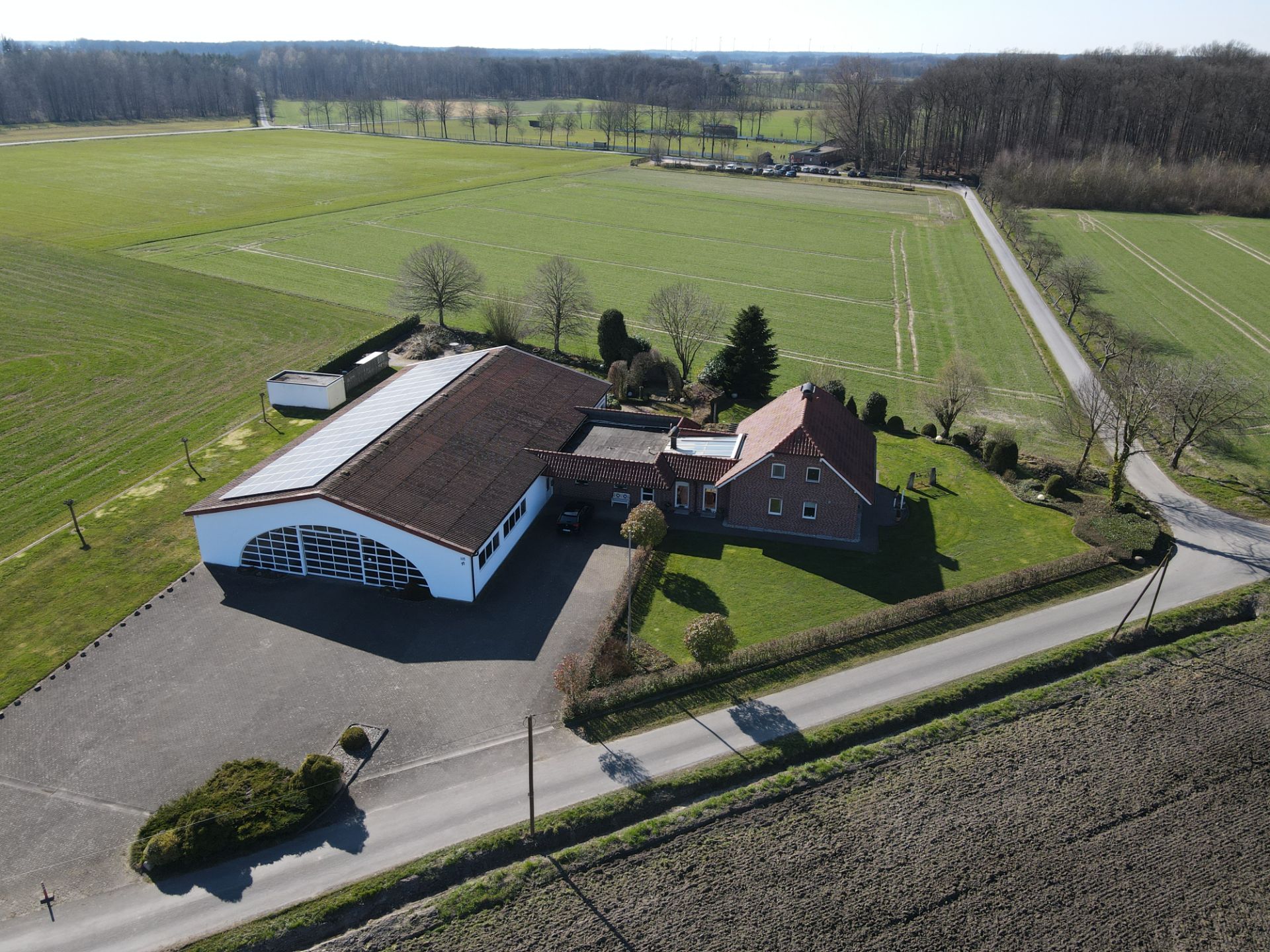 Drohnensicht auf ein Wohnhaus mit großem Nebengebäude und Garten, umgeben von Feldern.