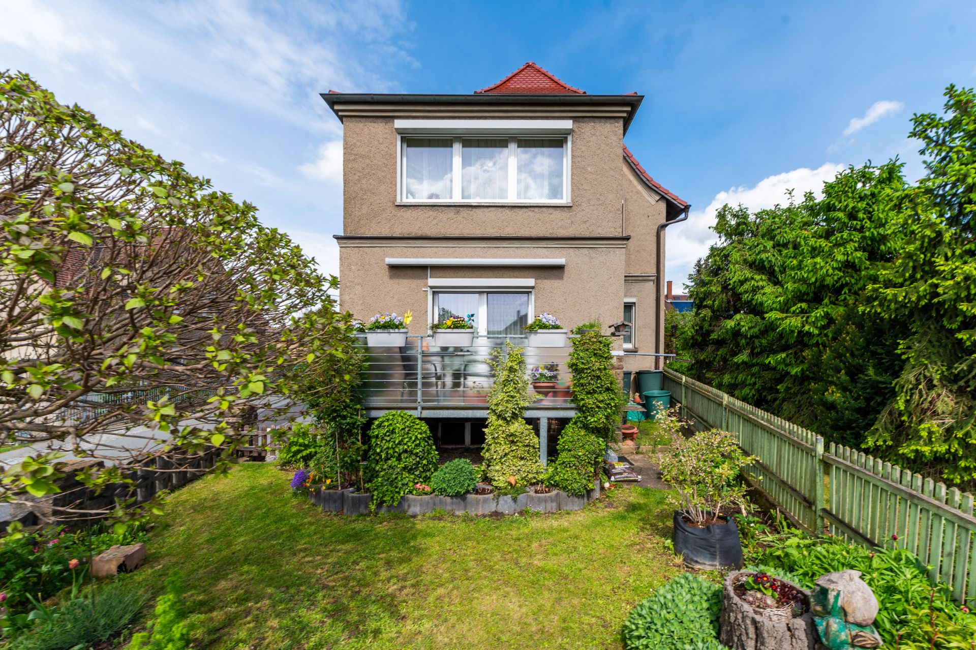 Zweistöckiges Wohnhaus mit Balkon und Garten, umgeben von Bäumen, aufgenommen bei Tageslicht.