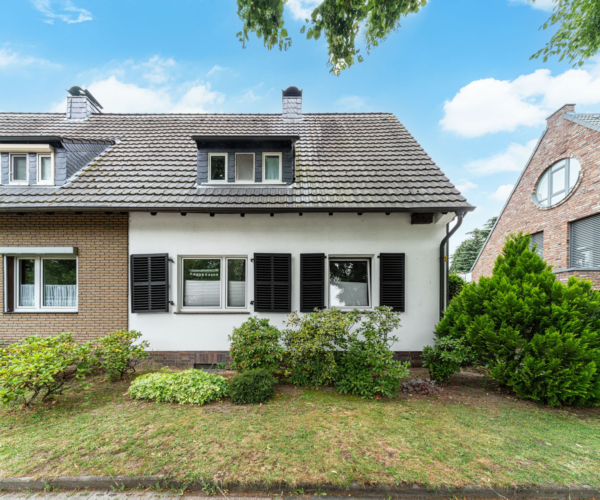 Außenansicht eines Doppelhauses mit Vorgarten und schwarzen Fensterläden.