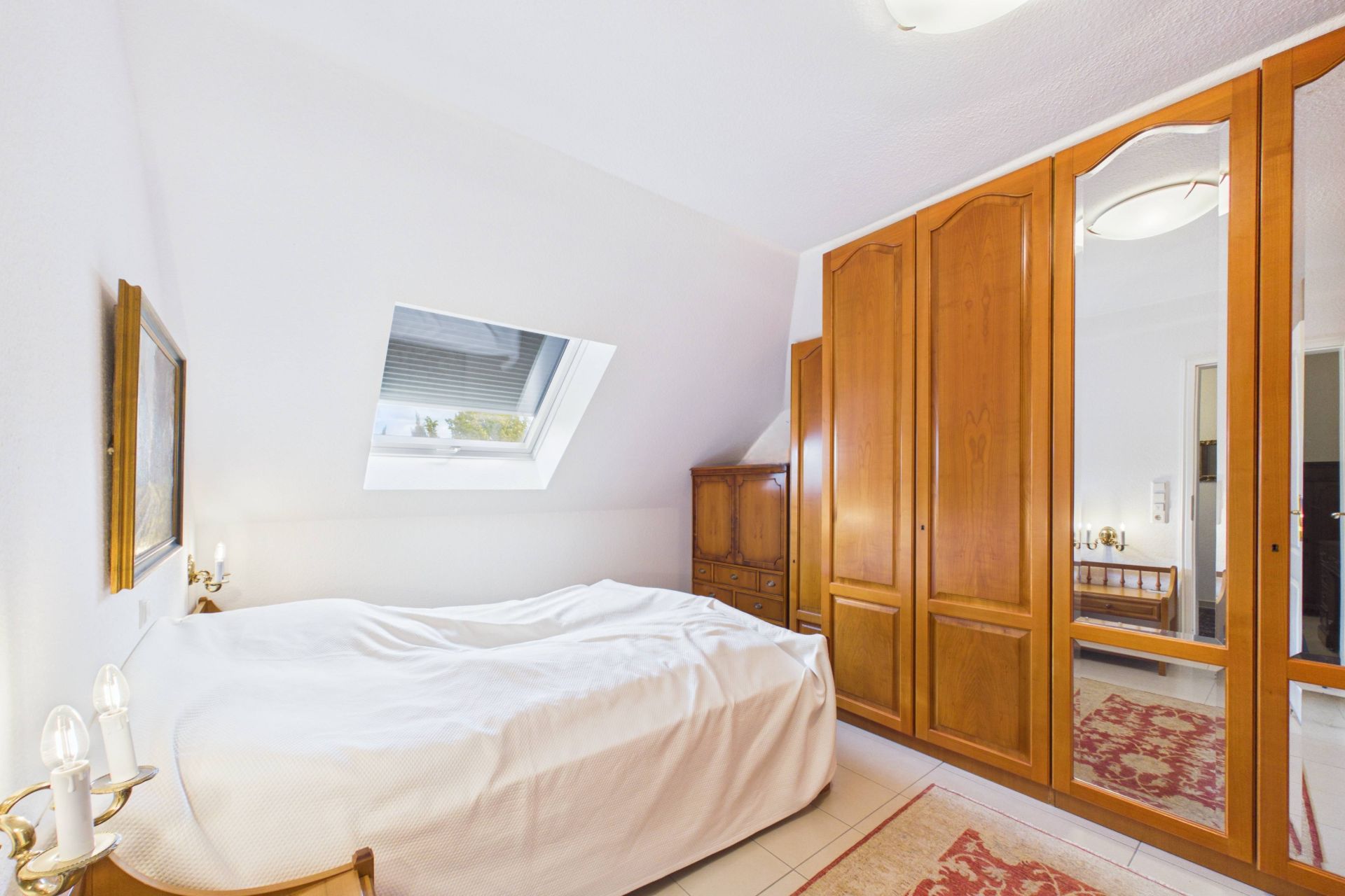 Helles Schlafzimmer mit Doppelbett, Holzschrank mit Spiegel und Dachfenster.