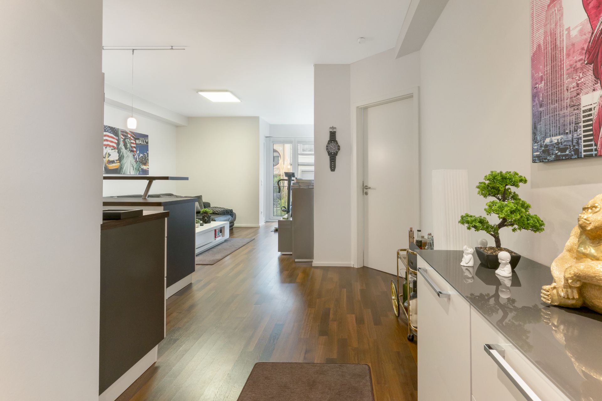 Moderner Flur mit Holzboden, weißen Wänden, Dekoration und Blick ins Wohnzimmer.