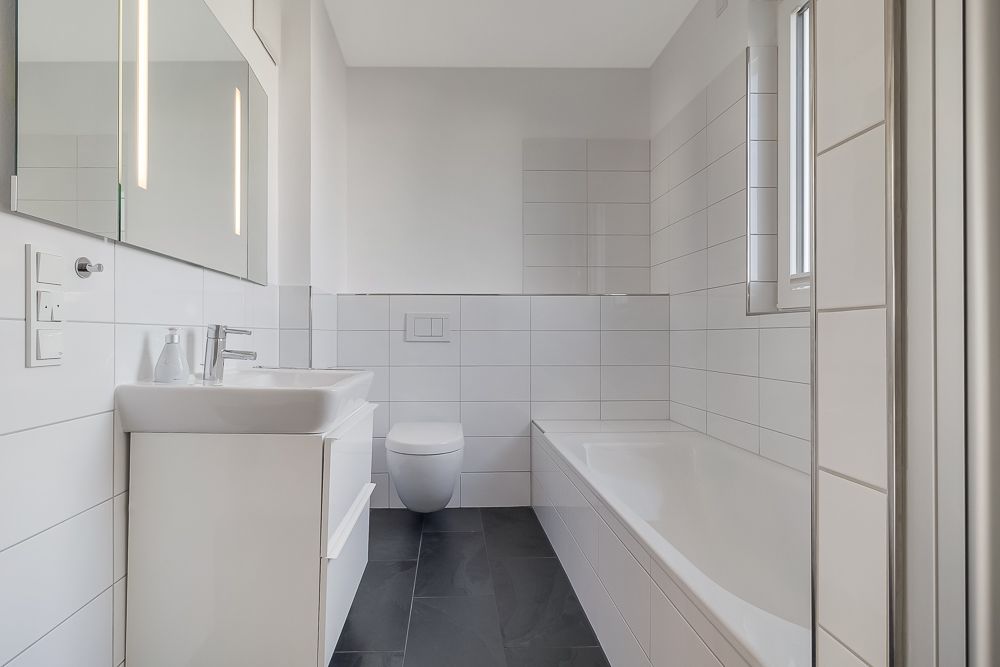 Modernes Badezimmer mit Badewanne, Waschbecken, wandhängender Toilette und großem Spiegel.