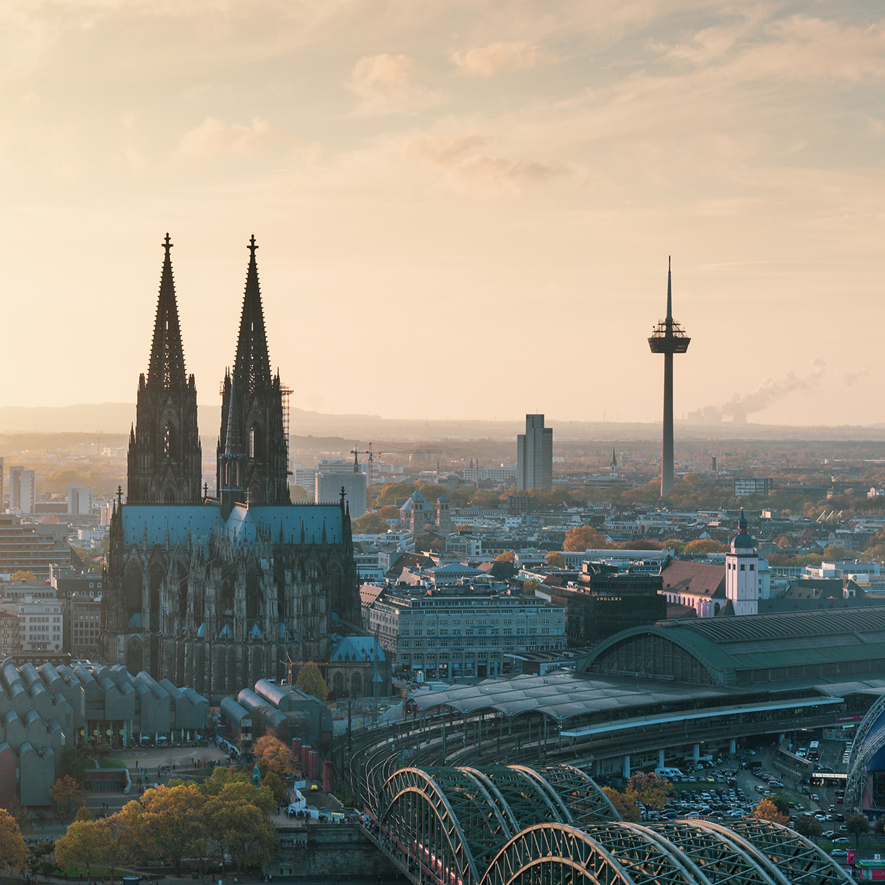 Stadtpanorama mit großer gotischer Kirche, Fernsehturm und Bahnhofsgebäude bei Sonnenuntergang.