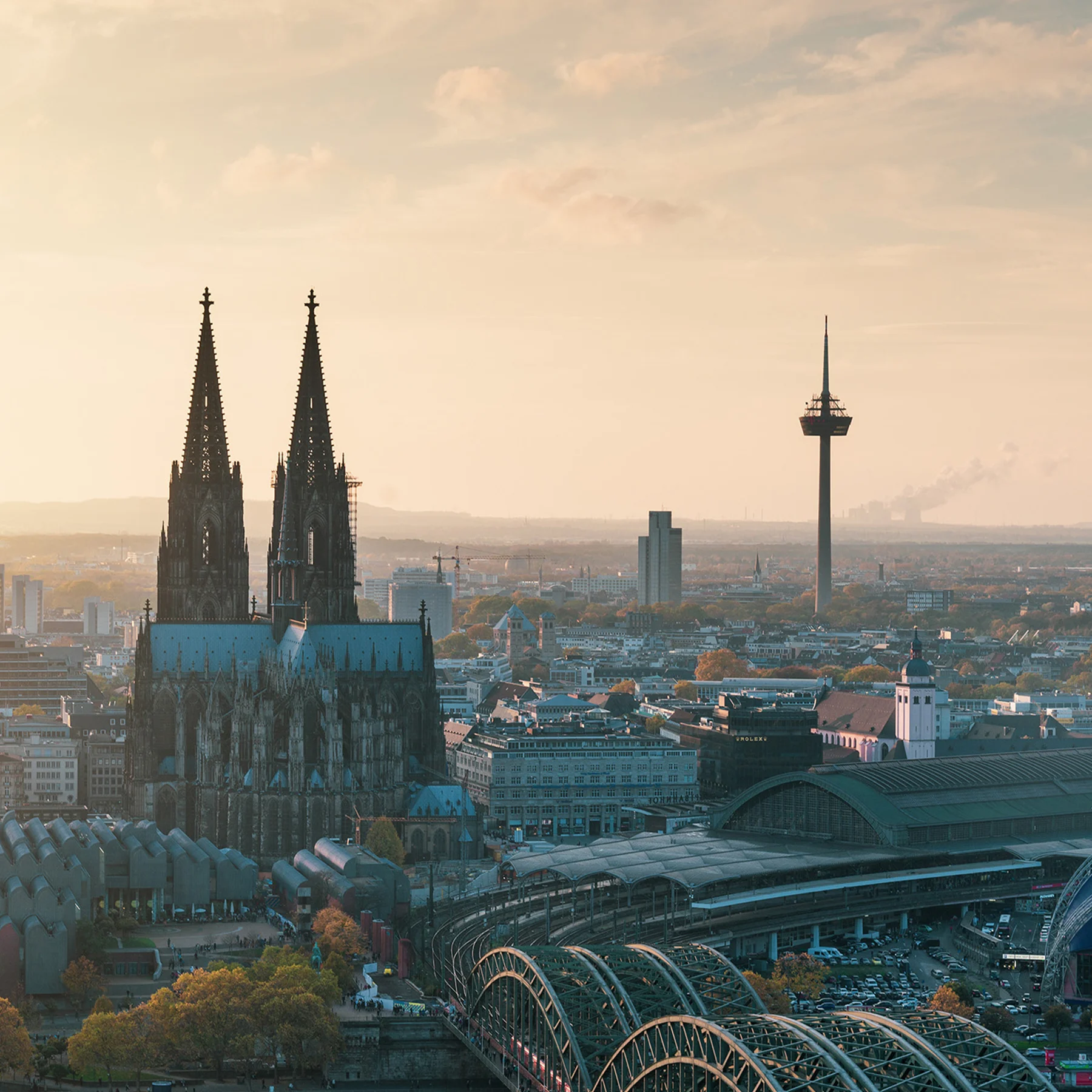 Stadtpanorama mit großer gotischer Kirche, Fernsehturm und Bahnhofsgebäude bei Sonnenuntergang.