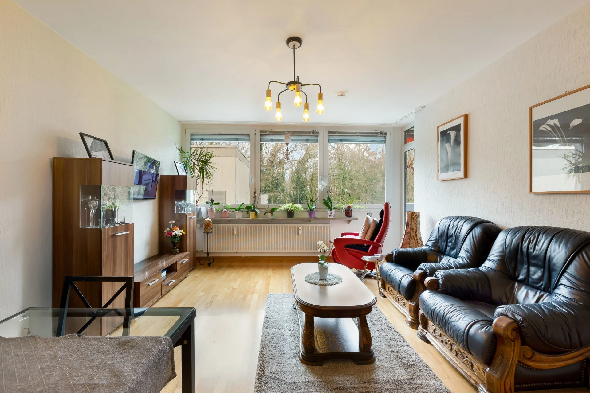 Helles Wohnzimmer mit Ledersofa, Sessel, Holztisch, TV-Schrank und großen Fenstern.