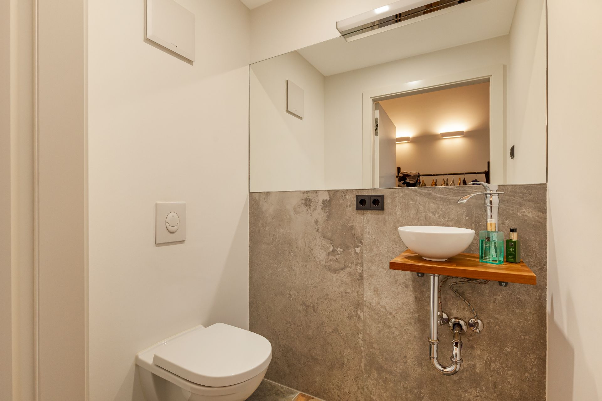 Modernes Gäste-WC mit Wandtoilette, Waschbecken auf Holzplatte und großem Spiegel.