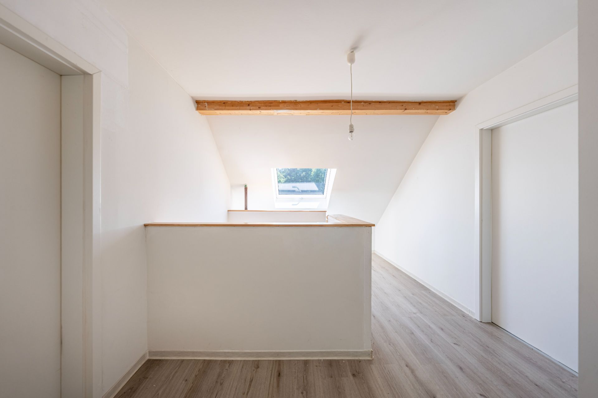 Heller Flur mit Holzfußboden, Dachschräge, Dachfenster und sichtbarem Holzbalken.