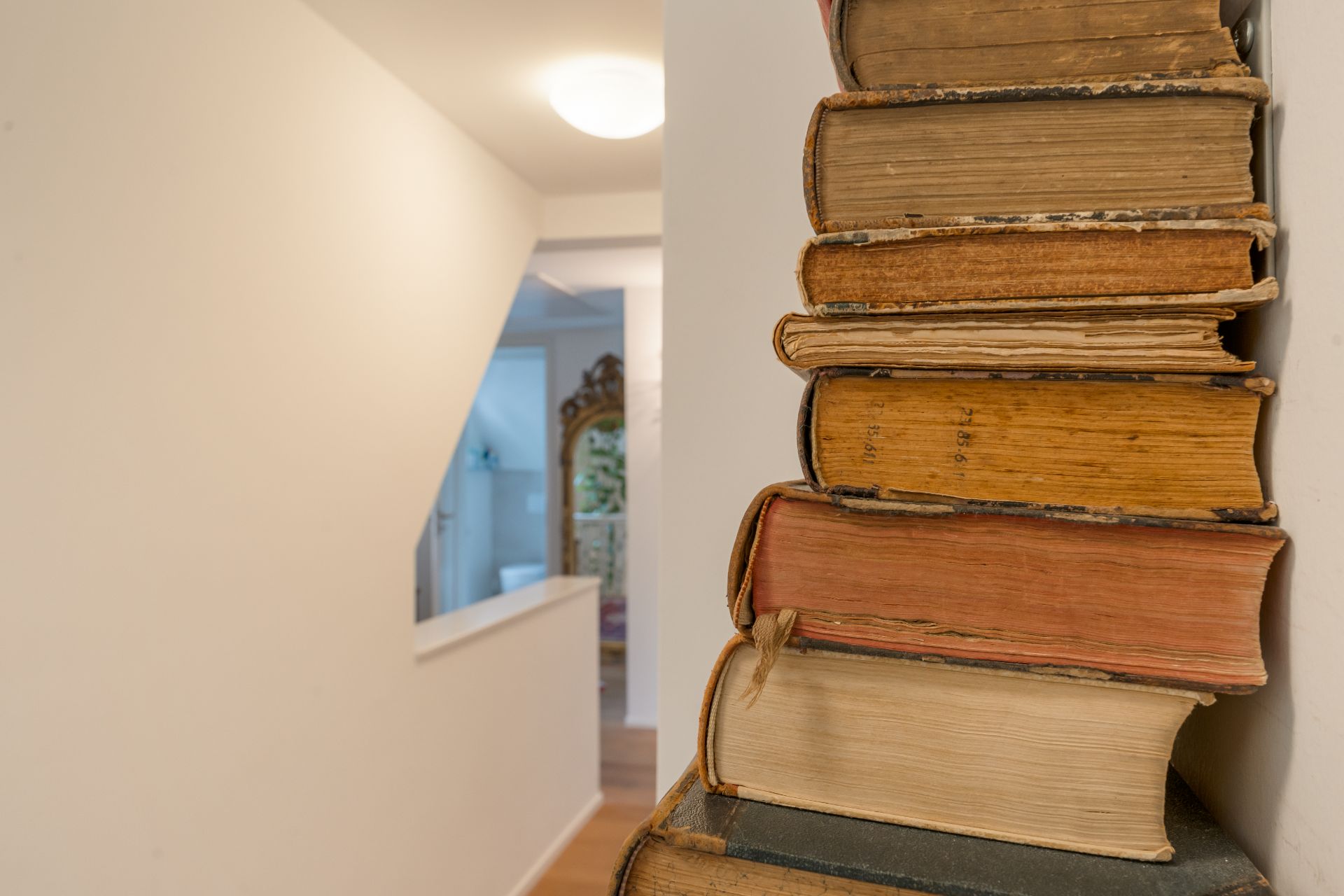 Ein Stapel alter Bücher steht neben einem hellen Flur mit Blick ins Badezimmer.