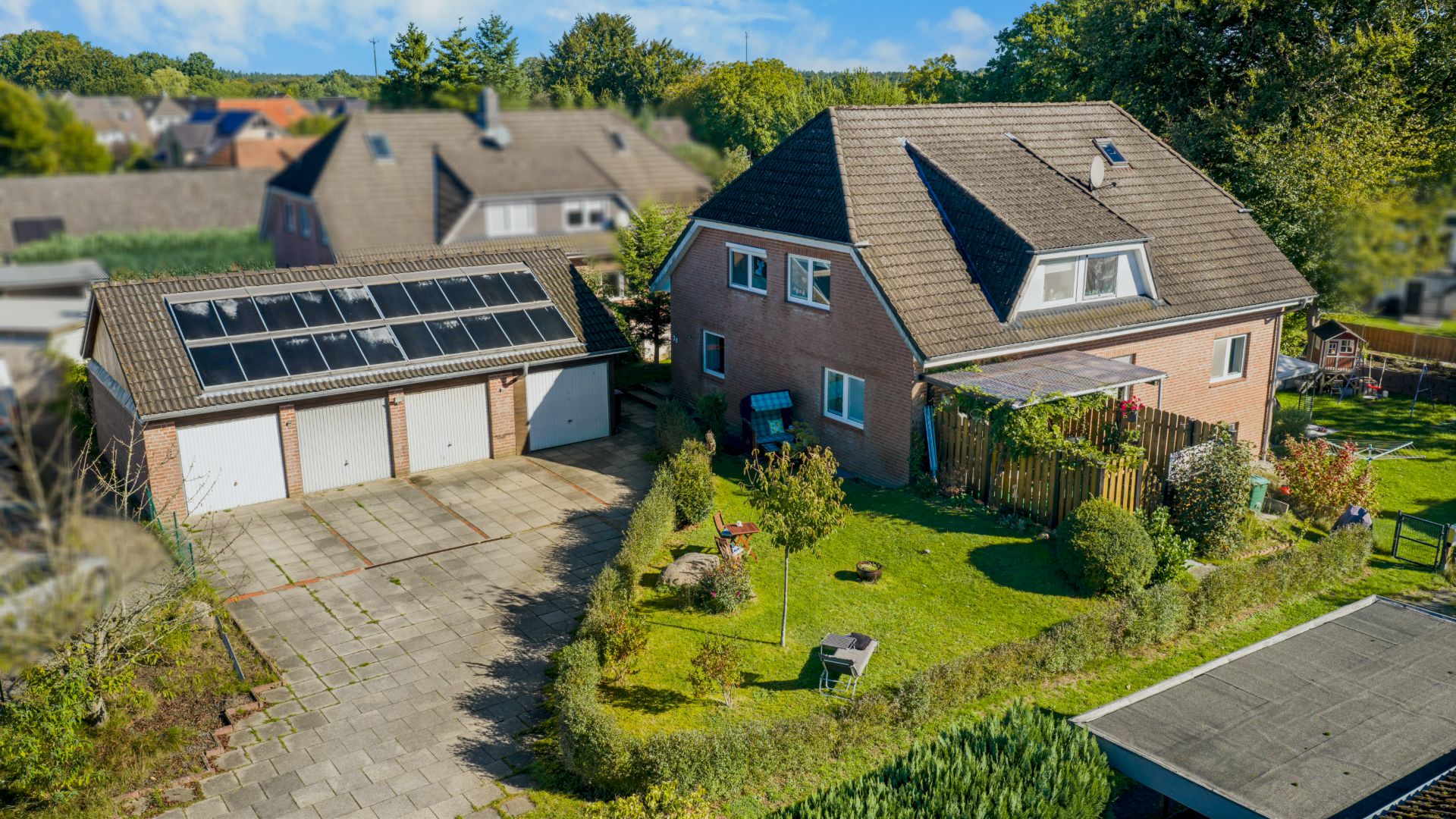 Zweistöckiges Wohnhaus mit Garten, Terrasse und separater Garage mit Solarpanelen.