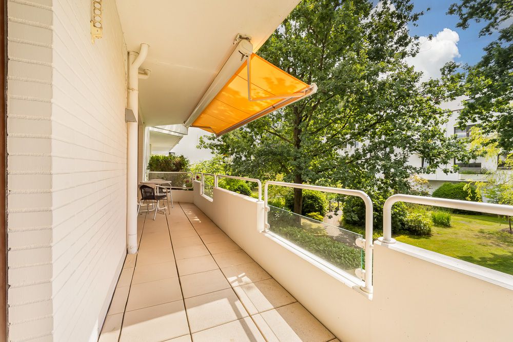 Großer Balkon mit gelber Markise, Blick ins Grüne, Tisch und Stühle vorhanden.