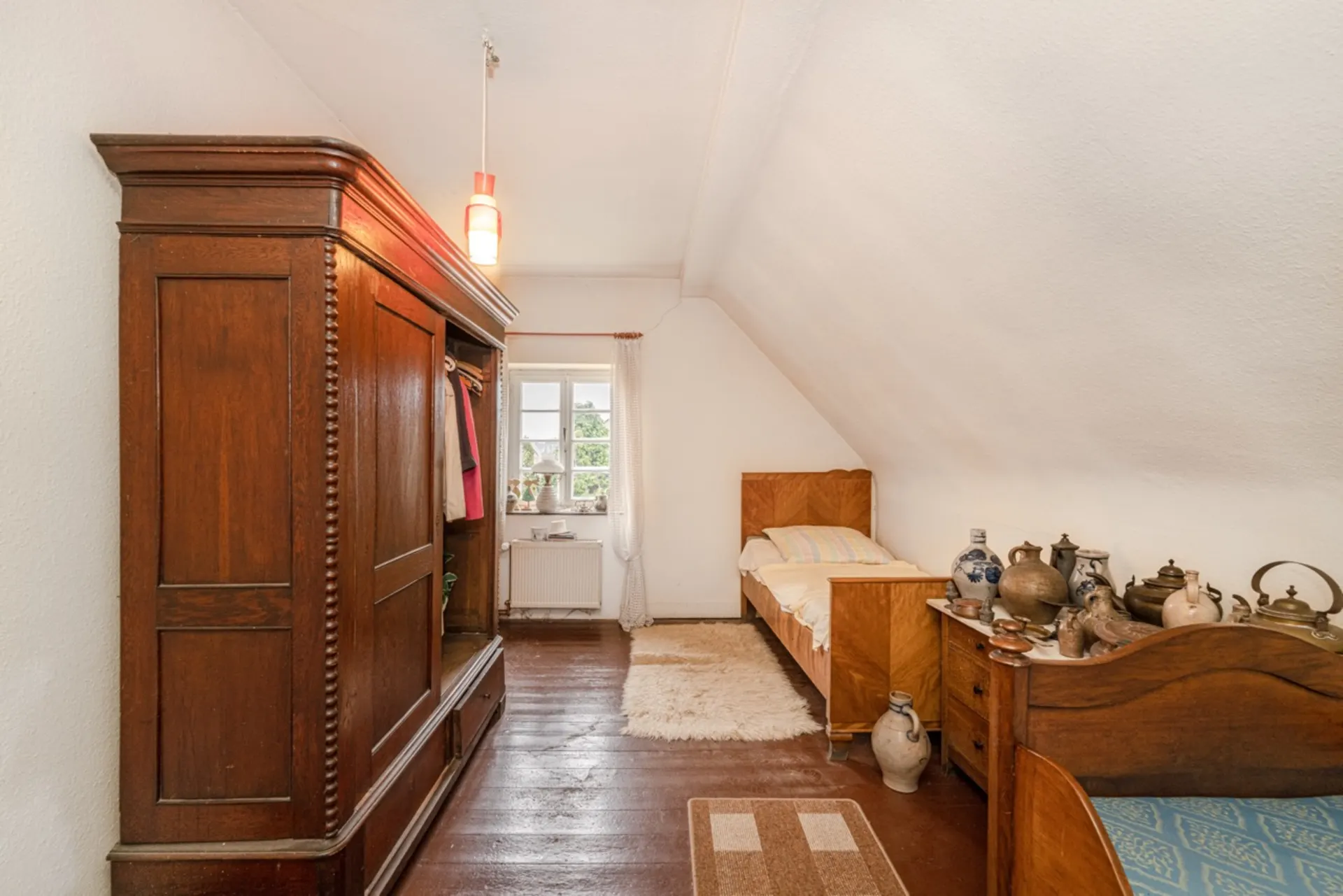 Schlafzimmer mit Holzbett, Kleiderschrank, Teppich und keramischen Krügen auf der Kommode.
