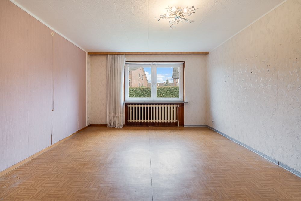 Leeres Zimmer mit Holzboden, großem Fenster, Heizung und heller Decke.
