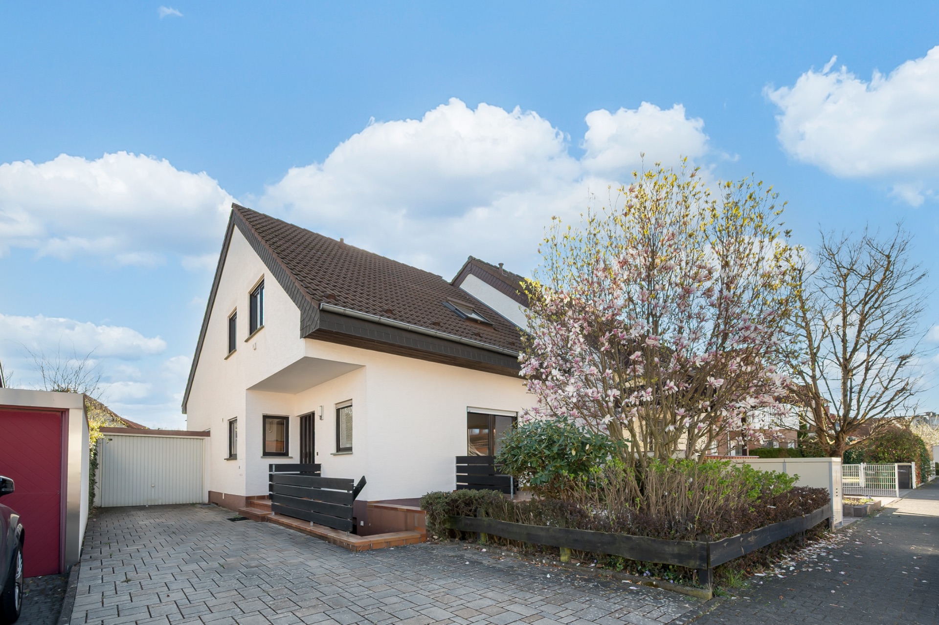 Zweistöckiges Einfamilienhaus mit braunem Dach, Einfahrt und blühendem Baum im Vorgarten.