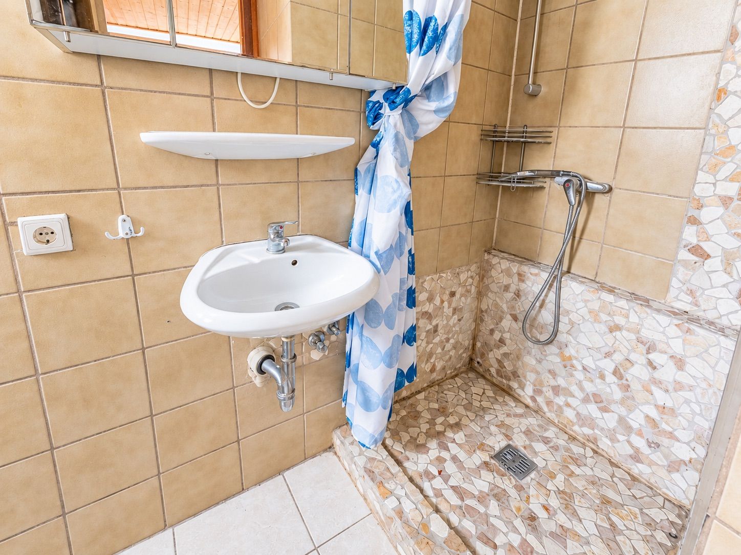 Kleines Bad mit Waschbecken und offener Dusche mit Mosaikfliesen und Duschvorhang.