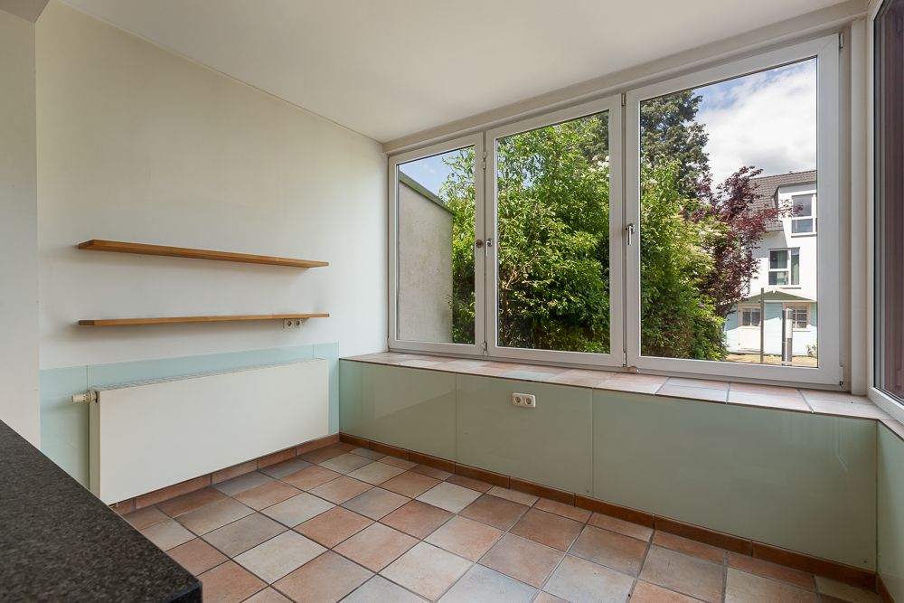 Heller Raum mit großen Fenstern, zwei Wandregalen und Fliesenboden.