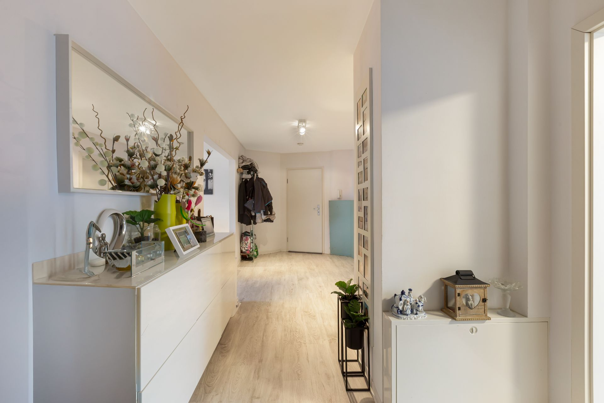 Heller Flur mit Kommode, Spiegel, Pflanzen und Jacken an der Wand.