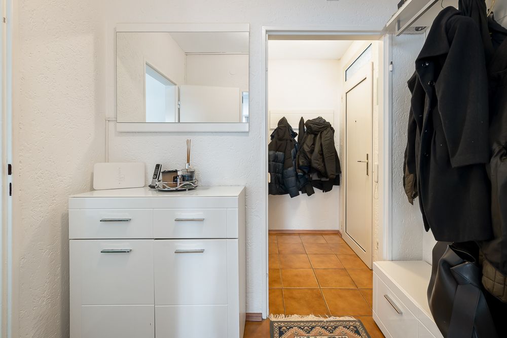 Heller Flur mit weißer Kommode, Spiegel und Garderobe mit Jacken.